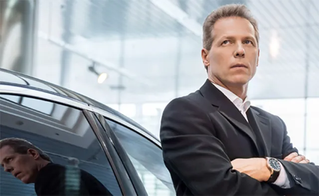 Professional driver in a suit standing beside a car